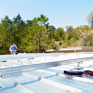 A worker installs aluminum rails on a metal roof to prepare for a solar panel installation