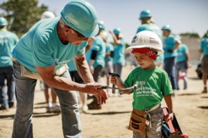 Volunteer shows hammer to small boy at Habitat build site